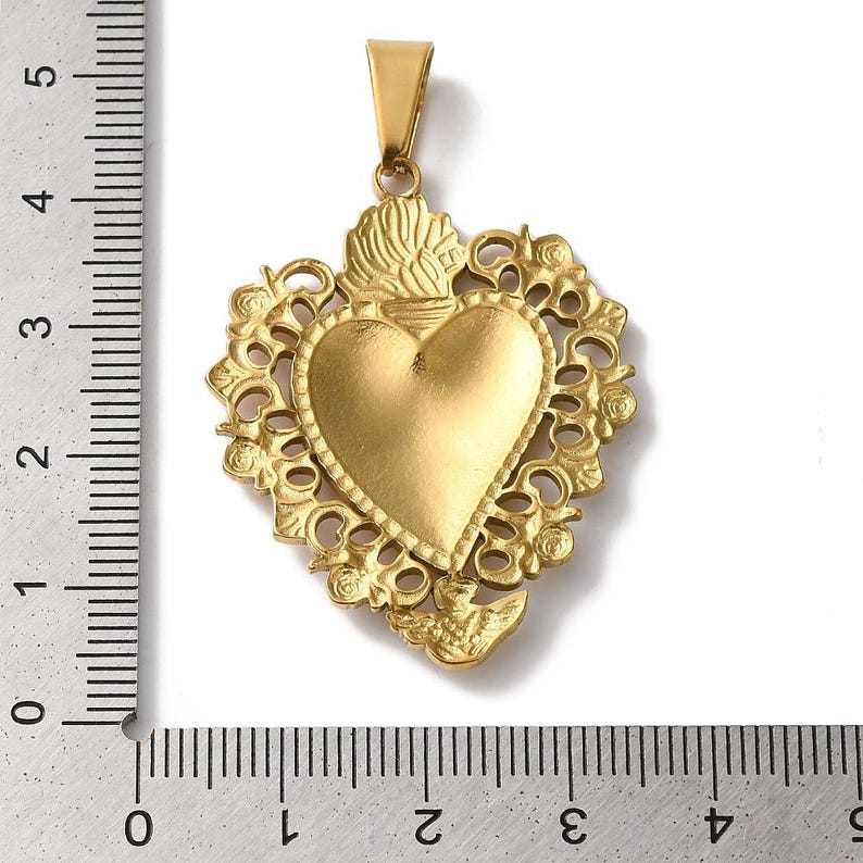 K&ouml;nnte beinhalten: Goldfarbener Anh&auml;nger mit herzf&ouml;rmigem Mittelteil, umgeben von einem verzierten Rand im Filigranstil. Der Anh&auml;nger hat eine &Ouml;se zum Anbringen an einer Kette. Der Anh&auml;nger ist etwa 5 cm lang.