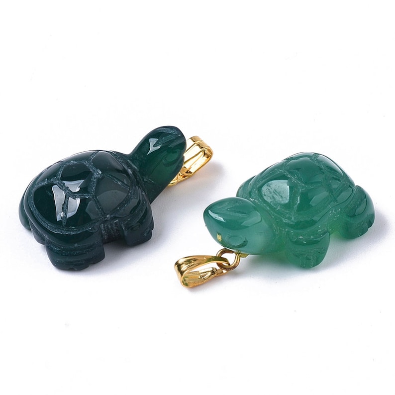 May include: Two green jade turtle pendants with gold-tone bail. The turtles are carved in a detailed design and have a smooth, polished finish.