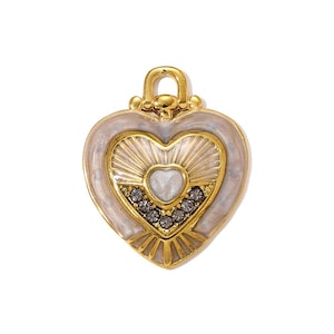 May include: A gold-colored heart-shaped pendant with a white enamel border. The pendant features a sunburst design and is embellished with small, dark gray crystals. A small loop is at the top for attaching to a chain.