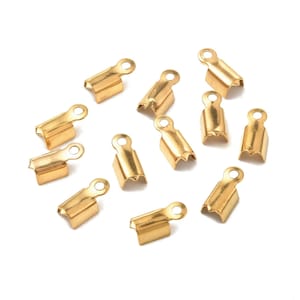 May include: A group of 12 gold-colored metal cord end caps. The caps have a small loop at the top and a scalloped edge.