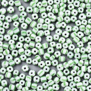 May include: A large quantity of white and green glass beads. The beads are small and round with a single green stripe around the middle.