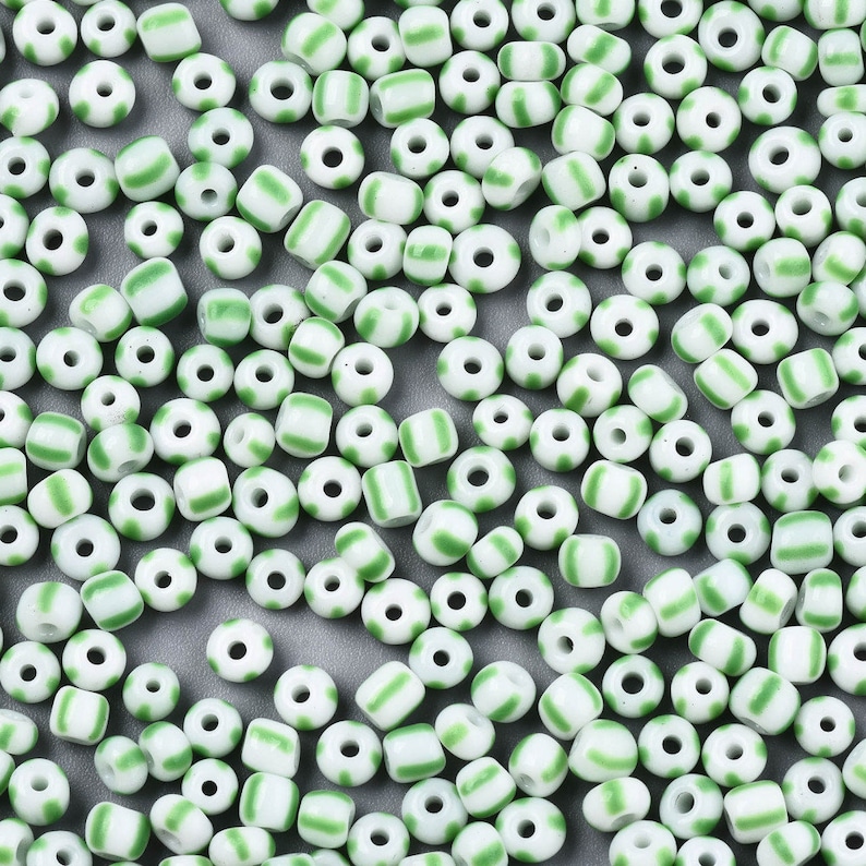 May include: A large quantity of white and green glass beads. The beads are small and round with a single green stripe around the middle.