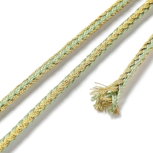 May include: A close-up of a green and gold braided cord. The cord is made of a soft, woven fabric with a metallic gold thread running through it.