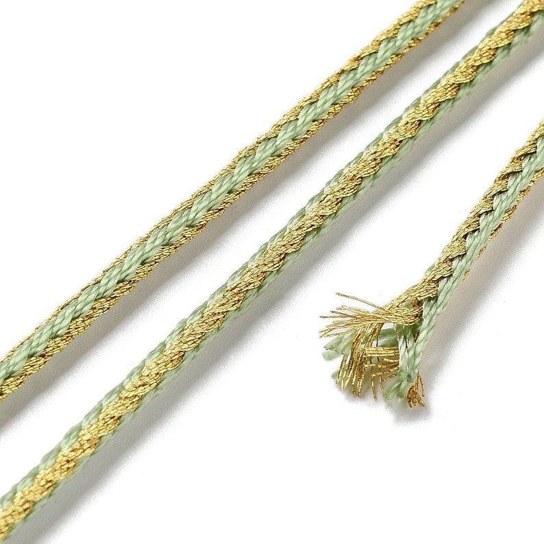 May include: A close-up of a green and gold braided cord. The cord is made of a soft, woven fabric with a metallic gold thread running through it.