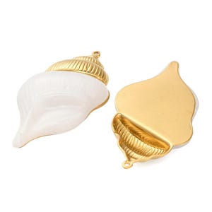 May include: Two seashell pendants. One is a white shell with a gold-colored top. The other is a gold-colored shell with a white interior. Both have a small loop for hanging.