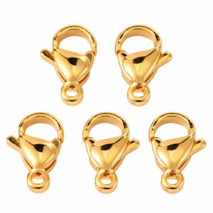May include: Five gold-toned metal lobster claw clasps arranged in a pattern. Each clasp features a smooth, reflective surface, a spring-loaded mechanism, and a circular loop at the base for attachment to jewelry or other craft projects.