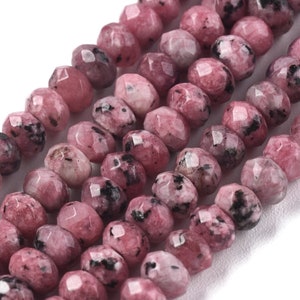 May include: A strand of pink and black faceted gemstone beads. The beads are irregularly shaped and have a speckled appearance.