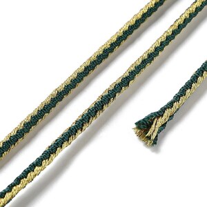 May include: A close-up of green and gold braided trim. The trim is made of a woven fabric with a herringbone pattern.