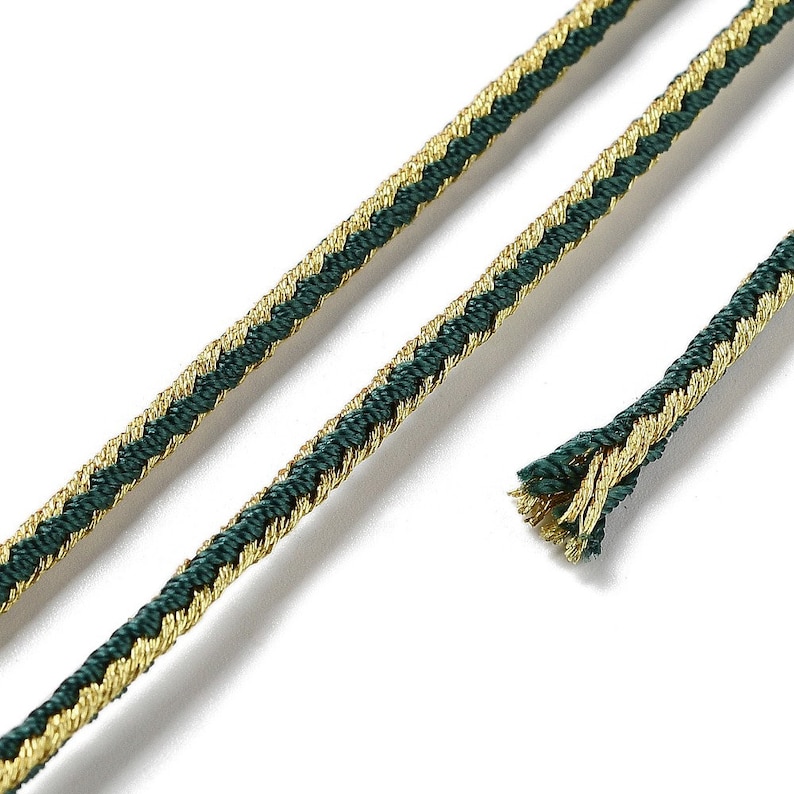 May include: A close-up of green and gold braided trim. The trim is made of a woven fabric with a herringbone pattern.