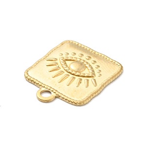 K&ouml;nnte beinhalten: Goldfarbener Metallanh&auml;nger mit quadratischer Form und einem gepr&auml;gten Augenmotiv. Das Auge hat ein detailliertes Design mit einem Kreis um die Pupille und strahlenden Linien um das Auge.