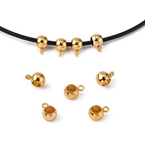 Könnte beinhalten: Goldfarbene Metallperlen-Endstücke mit Schlaufe zur Schmuckherstellung. Mehrere Perlen sind abgebildet, einige an einer schwarzen Kordel befestigt. Die Perlen sind rund mit einer kleinen Schlaufe zum Befestigen.