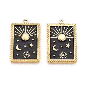 May include: Two gold-toned rectangular pendants with black enamel detailing. Each pendant features a sunburst design, a central sun, crescent moon, stars, and a smaller sun. The pendants have a beaded border and a loop for hanging.
