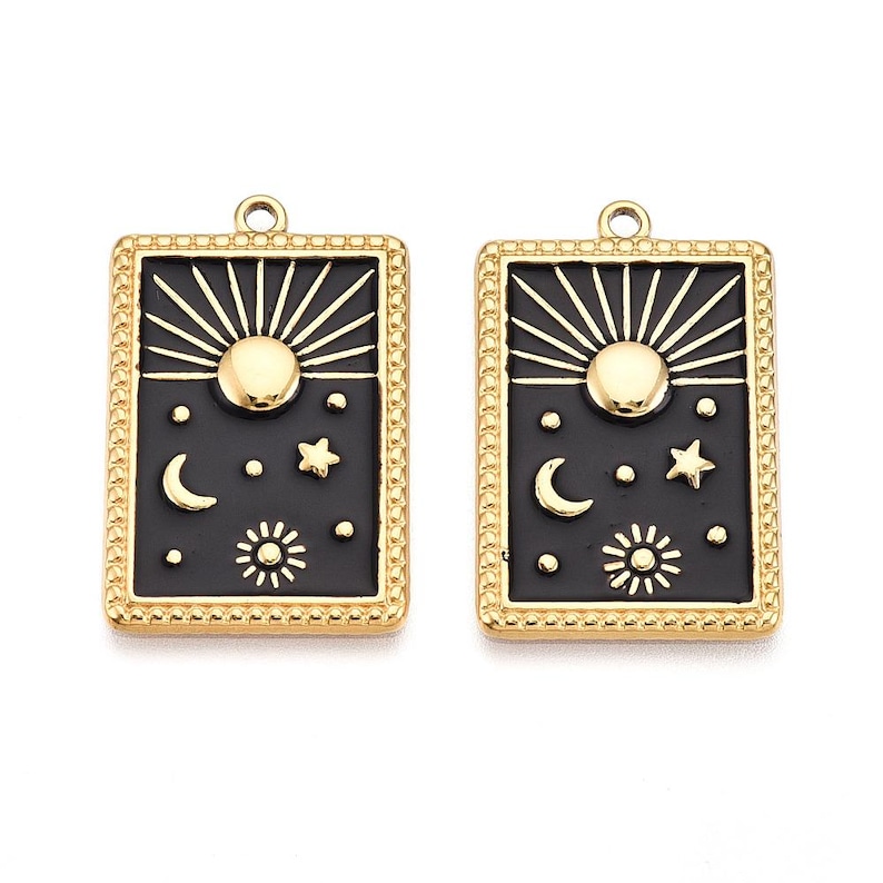 May include: Two gold-toned rectangular pendants with black enamel detailing. Each pendant features a sunburst design, a central sun, crescent moon, stars, and a smaller sun. The pendants have a beaded border and a loop for hanging.