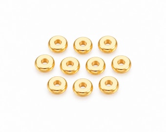 Könnte beinhalten: Eine Ansammlung von neun kleinen, runden, goldfarbenen Metallperlen, die in einer Gruppe angeordnet sind. Jede Perle hat eine glatte, polierte Oberfläche mit einem zentralen kreisförmigen Loch, was ein einheitliches Erscheinungsbild erzeugt.