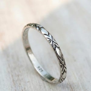 May include: A silver ring with an etched geometric pattern. The ring is thin and has a repeating design of intersecting lines and diamond shapes. The number "925" is stamped on the inside of the ring.