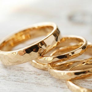 Puede incluir: Primer plano de varios anillos dorados con textura martillada. Los anillos están apilados, mostrando sus superficies brillantes y reflectantes. Los anillos probablemente están hechos de oro o metal dorado.