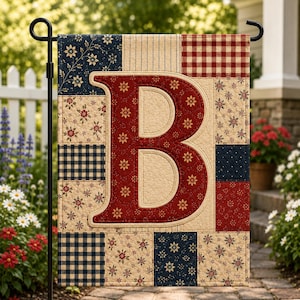 May include: A decorative garden flag featuring a large red letter "B" with floral accents, set against a patchwork background of navy, cream, and red fabrics. The flag is displayed on a black metal stand, perfect for outdoor decor.