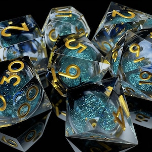 Puede incluir: Un conjunto de dados transparentes de múltiples caras con números dorados y un diseño interior turquesa y azul. Los dados están dispuestos sobre una superficie negra reflectante, perfectos para juegos de mesa.