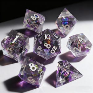 Peut inclure: Ensemble de sept dés polyédriques pour jeux de rôle. Les dés transparents présentent un design intérieur violet et argenté. Chaque dé est numéroté en argent. Les dés sont disposés sur une surface blanche.