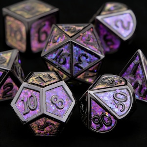 Pode incluir: Um conjunto de dados iridescentes com uma moldura metálica prateada. Os dados têm um esquema de cores roxo, dourado e azul. Os números estão em uma fonte cinza escuro. Os dados são para jogos de tabuleiro.