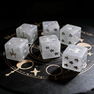 May include: Six translucent dice with star cutouts and etched zodiac symbols. The dice are gray and sit on a dark surface with astrological symbols. The dice are a unique set for tabletop games or collectors.