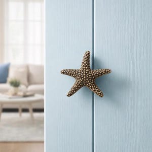 May include: A bronze-colored starfish-shaped cabinet knob with a textured surface. The knob is mounted on a light blue cabinet door. The knob is a decorative accent for coastal or nautical-themed decor.