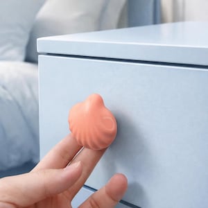 Peut inclure: Gros plan d'un bouton de tiroir en forme de coquillage pêche. La poignée est tenue contre un tiroir bleu clair. Le motif de coquillage présente des arêtes détaillées et une finition lisse et brillante. Décoration intérieure.