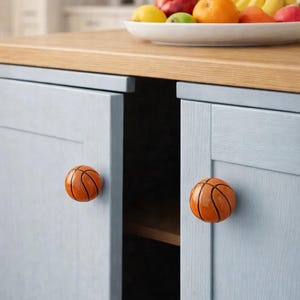 May include: Light blue cabinet doors with orange basketball-shaped knobs. A wooden countertop supports a white bowl filled with fruit. The cabinet doors are closed, and the knobs are centered on each door.