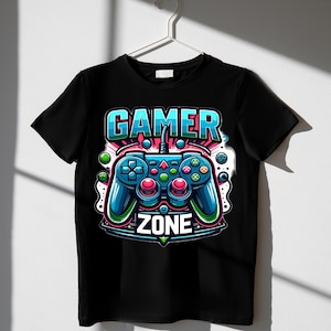 May include: Black t-shirt with a colourful graphic of a video game controller and the words "GAMER ZONE". The controller is blue, red, and green, with a detailed illustration. The t-shirt is hanging on a white hanger.