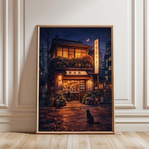 以下が含まれることがあります： 夜の日本のレストランの額入りアートプリント。建物は温かい照明で、日本語の看板があります。黒い猫が石畳の通りに座っています。アートワークは、都市のスカイラインと三日月を背景に設定されています。