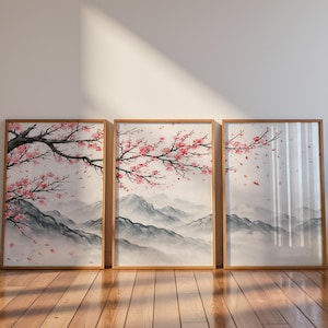 以下が含まれることがあります： 桜の花が咲く穏やかな風景を描いた、額入りのアートプリント3枚。霧に包まれた山脈と、ピンク色の花が咲く枝が描かれています。フレームは明るい色の木材でできており、プリントは木の床に展示されています。