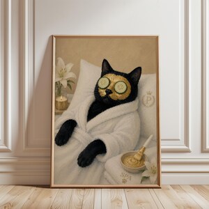 May include: A framed wall art print featuring a black cat wearing a white bathrobe and a gold facial mask with cucumber slices over its eyes. The cat rests against a pillow with a gold crown and letter P logo, next to a candle and a bowl of mask.