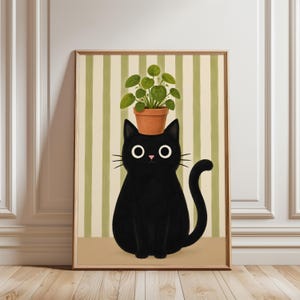 May include: A framed wall art print featuring a solid black cat with large white eyes sitting upright. A small green plant in a terracotta-colored pot is balanced on the cat's head. The background consists of vertical light green and cream stripes.