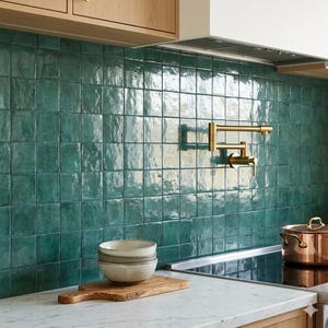 May include: A kitchen scene featuring a teal tile backsplash, a gold faucet, and a marble countertop. Two stacked bowls sit on a wooden cutting board. A copper pot rests on the stovetop, and wooden cabinets are visible.