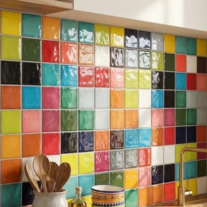 May include: A colorful kitchen backsplash composed of square tiles in various colors, including yellow, green, red, and blue. Wooden spoons in a ceramic jar, a bottle of oil, and a decorative bowl sit on a wooden countertop.