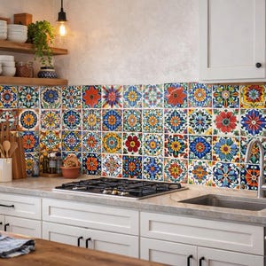 May include: A kitchen with a colorful tile backsplash featuring floral patterns in red, blue, yellow, and green. White cabinets, a stainless steel sink, and a gas cooktop are visible. Wooden shelves hold white dishes and decorative items.