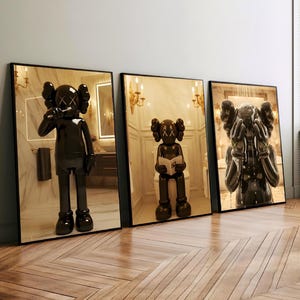 May include: Three framed art prints showcasing black sculptures in bathroom scenes. One sculpture brushes its teeth, another reads, and the third is under a shower. The art has a glossy finish and is displayed on a wooden floor.