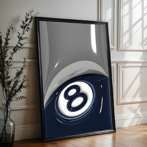 May include: Framed art print featuring a glossy, abstract design of the number eight in white against a navy blue and gray background. The artwork is encased in a black frame and leans against a white wall.