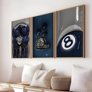 May include: Three framed art prints with a modern design. The prints feature a blue and gray color scheme with abstract figures and a pool ball. The frames are a light brown color.