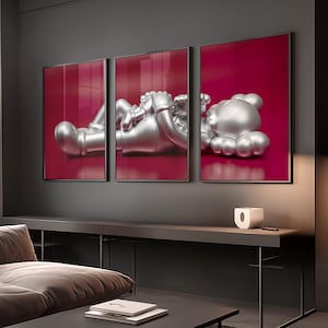 Pode incluir: Um tríptico de arte emoldurada com uma escultura prateada sobre um fundo vermelho profundo. A escultura retrata uma figura estilizada em uma pose relaxada. As molduras são pretas e a obra de arte é exibida em uma parede cinza.