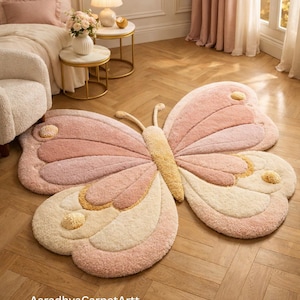 Large pastel butterfly-shaped tufted rug in blush pink, cream and soft yellow on a herringbone wood floor in a cozy bedroom, AaradhyaCarpetArtt.