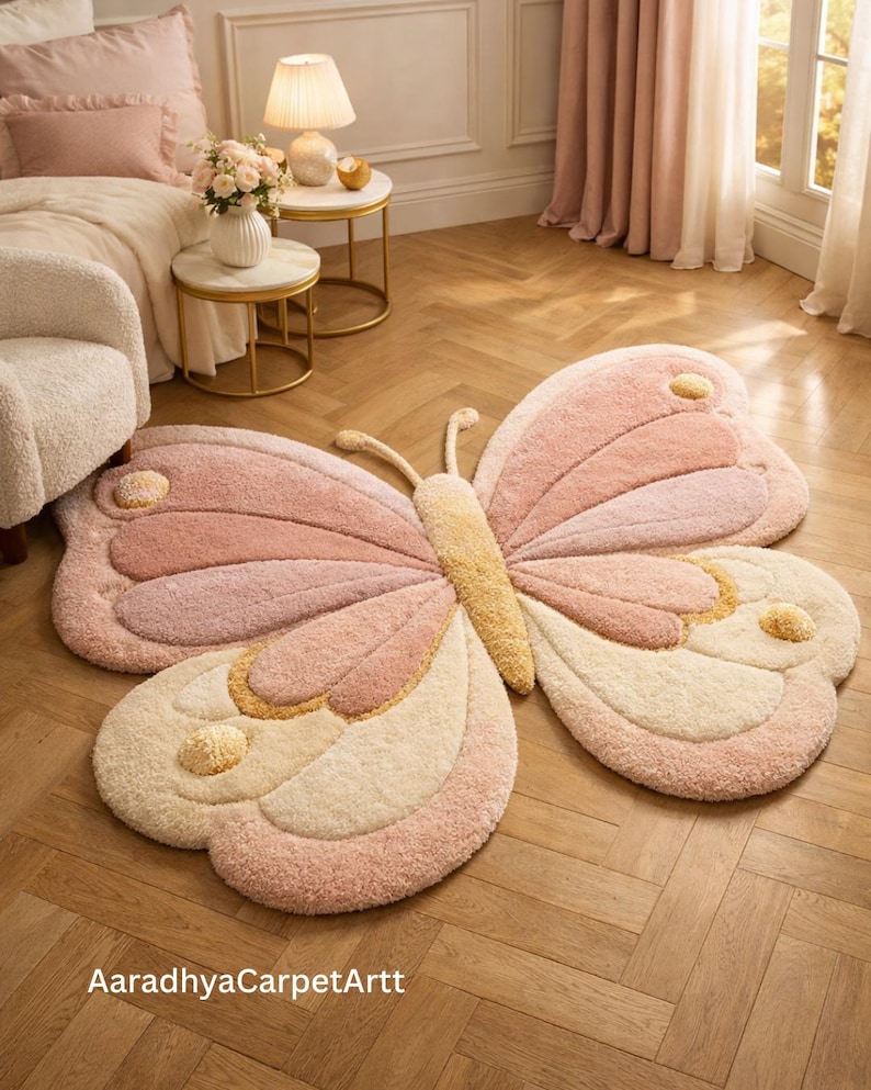 Large pastel butterfly-shaped tufted rug in blush pink, cream and soft yellow on a herringbone wood floor in a cozy bedroom, AaradhyaCarpetArtt.