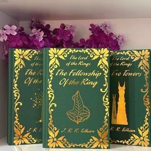 May include: Three green hardcover books titled The Lord of the Rings, The Fellowship of the Ring, and The Two Towers. Each book features gold foil lettering and intricate floral border designs, with specific gold leaf illustrations on the covers.