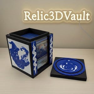 May include: A black and white card storage box with a blue wizard design and the text "Relic3DVault". The box has a removable lid with a blue and white circular design. The box is designed to hold trading cards.