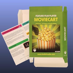 May include: A green cardboard box for the MovieCart feature film player, featuring a graphic of popcorn in a striped container and text including "4.9 Tindie.com Product Rating" and "www.lodefmode.com". An instruction sheet shows controller actions.