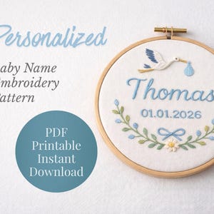 May include: Embroidered baby name pattern in a wooden hoop. The design features the name "Thomas" in light blue script, a stork carrying a bundle, and a floral wreath. The date 01.01.2026 is also included. The text "Personalized" and "Baby Name Embroidery Pattern" are displayed.