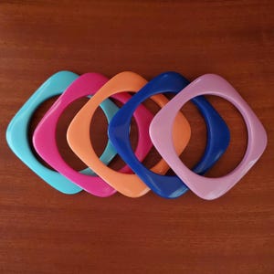 May include: A set of five square-shaped bangle bracelets in solid colours including turquoise, hot pink, orange, royal blue, and light purple. Each bangle features a smooth, rounded finish with a distinct four-sided geometric design.