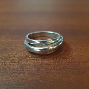 Peut inclure: Une bague de couleur argentée présentant un design à bandes superposées et entrelacées. La surface métallique est lisse et réfléchissante, créant une structure en boucle continue et interconnectée qui s'enroule pour former un bijou unique.