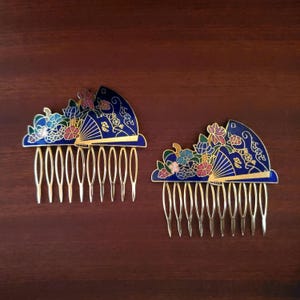 May include: Two gold-toned hair combs featuring a decorative fan-shaped top with deep blue enamel. The design includes colorful floral accents in shades of pink, green, and light blue, with gold outlines defining the intricate patterns on each piece.