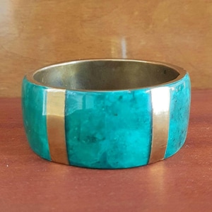 Può includere: Un bracciale largo turchese con due strisce verticali dorate. L'interno del bracciale è dorato. Questo bracciale audace è un accessorio sorprendente, perfetto per aggiungere un tocco di colore a qualsiasi outfit. Diametro: circa 6 cm.